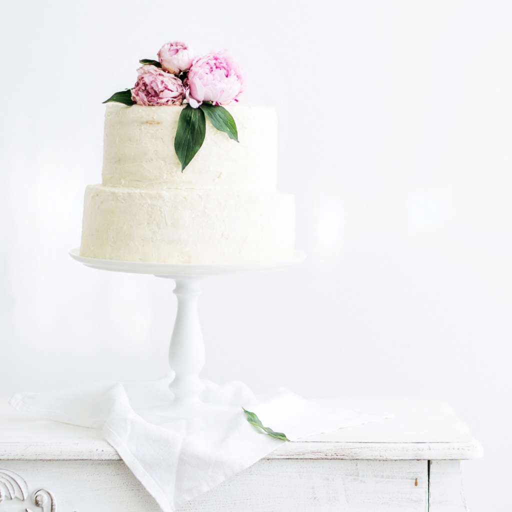 gâteau de mariage blanc surmonté de 3 pivoines roses et posé sur table. 12 astuces pour une organisation sans stress. Wedding Planner Ile de France. Paris en Noces 